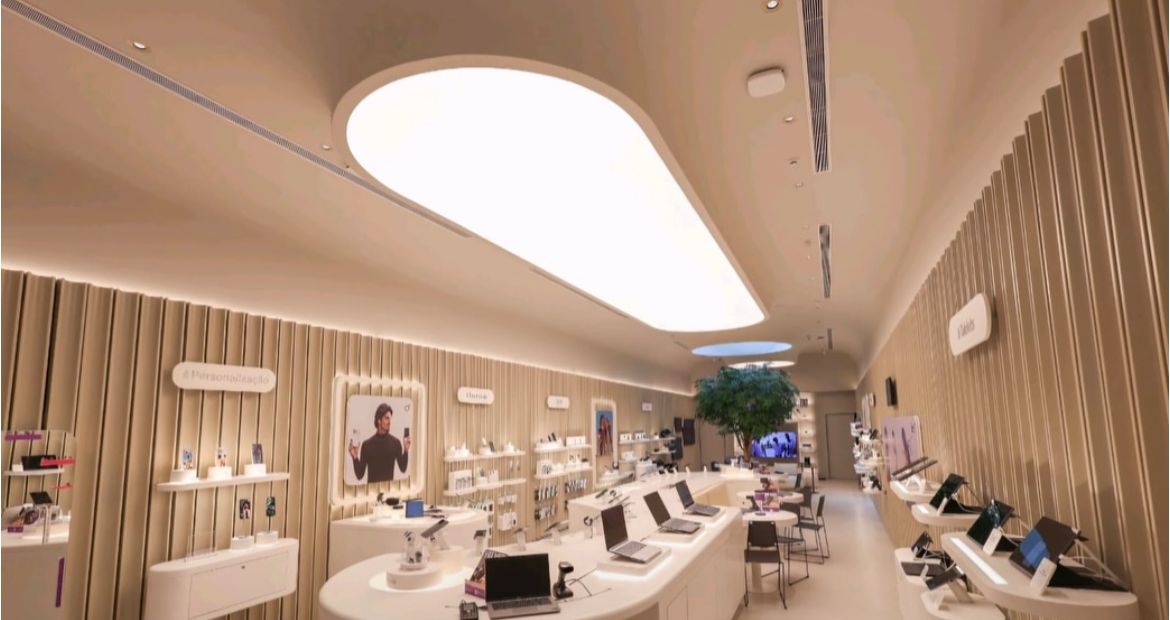 Corredor da loja com ilhas curvas em corian branco, painéis ripados e forro iluminado orgânico