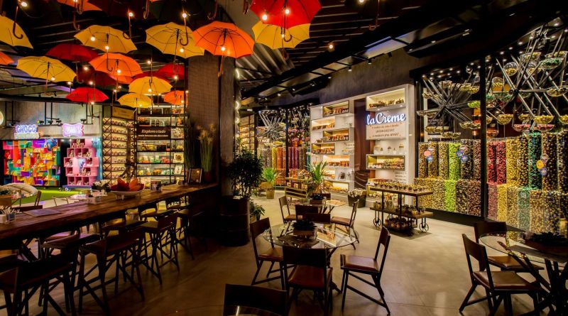 Cafeteria La Crème com teto de guarda-chuvas coloridos, bancada alta e ambiente lounge integrado