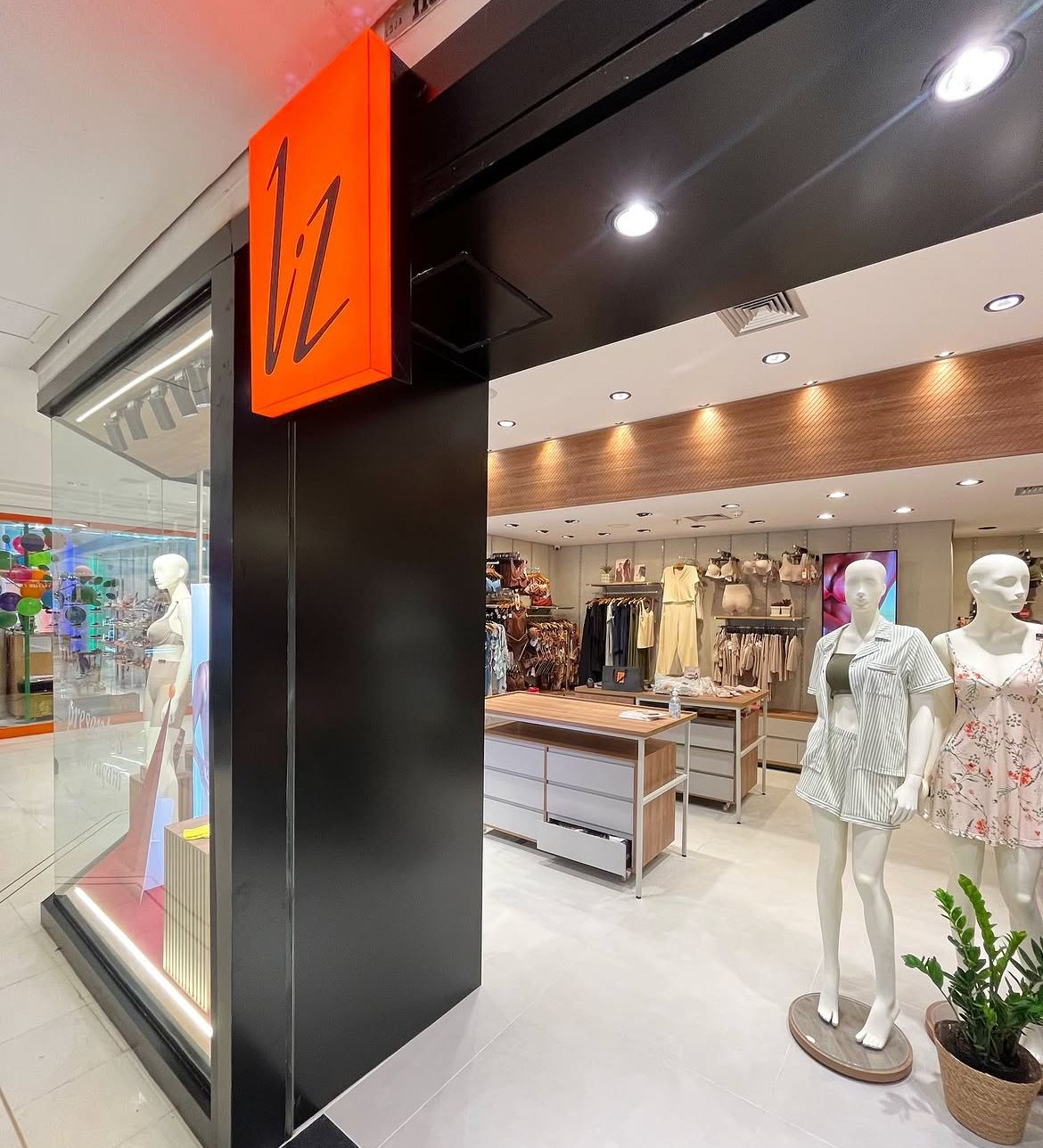 Fachada da loja Liz com testeira retroiluminada em vermelho e portal preto emoldurando o interior claro