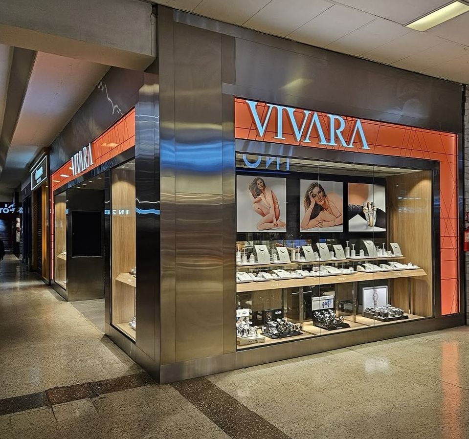 Fachada da loja Vivara com testeira retroiluminada laranja e revestimento em aço inox espelhado