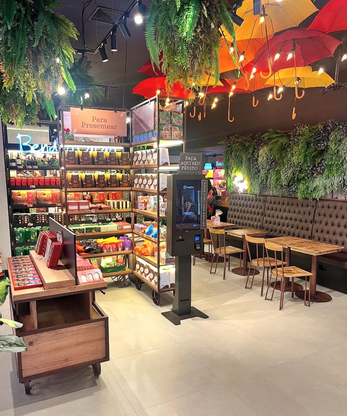Interior da loja Cacau Show com cafeteria, totem de autoatendimento e prateleiras rodantes