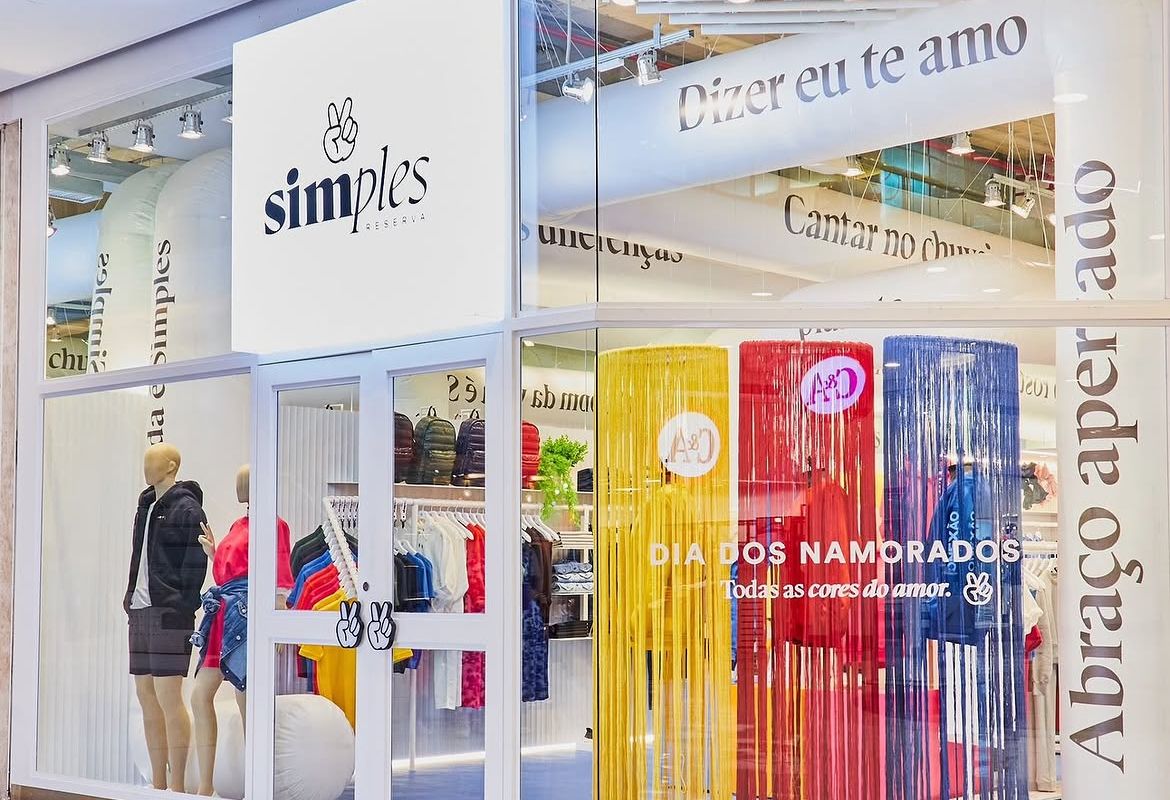Fachada da pop-up Simples Reserva com testeira branca, cortinas metálicas coloridas e tipografia aplicada